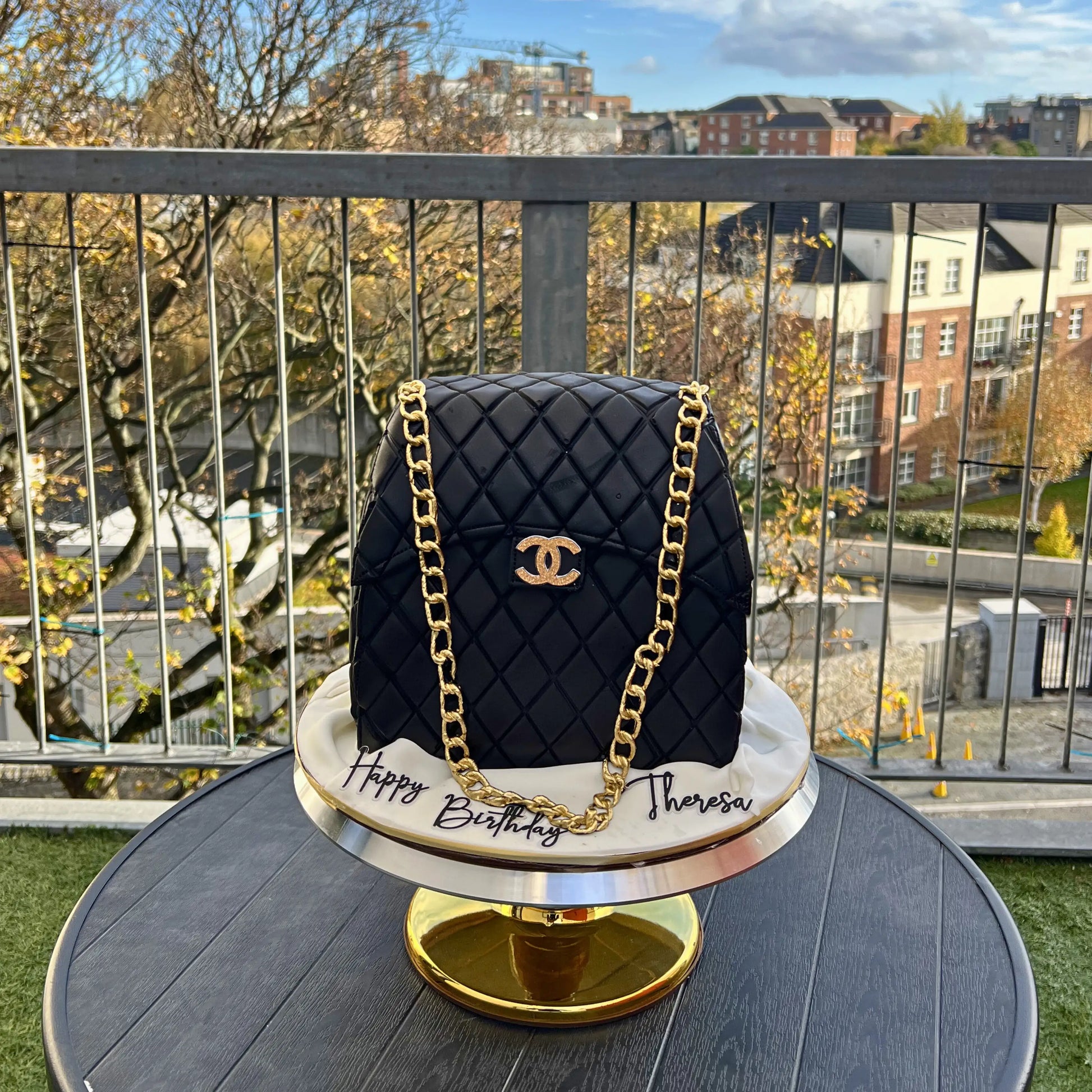 Black quilted handbag cake with gold chain on a stand outdoors