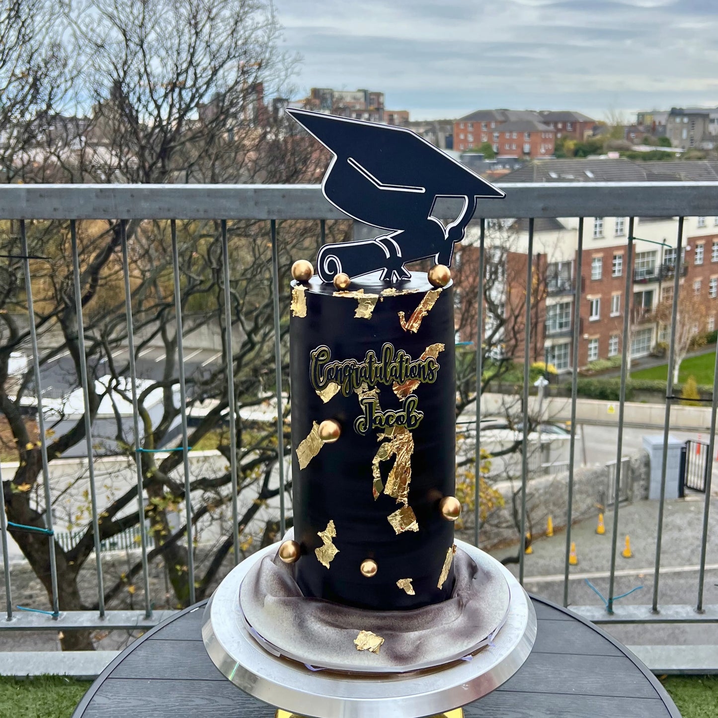 Graduation-themed cake with a topper on a balcony with a cityscape background