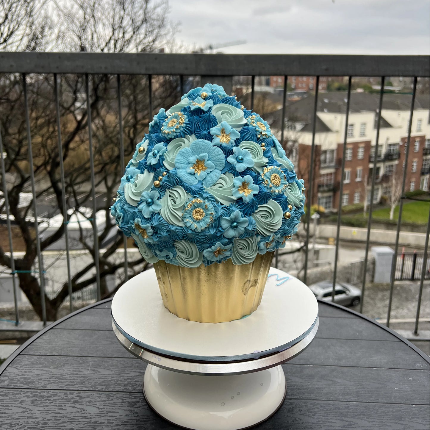 Large decorative cupcake with blue and green frosting on a stand outdoors.