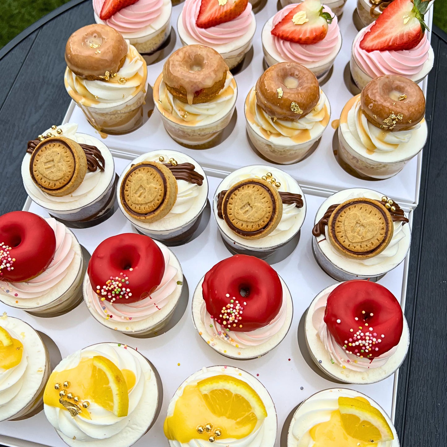 Assorted mini desserts including donut-shaped cookies and cupcakes on a white tray.