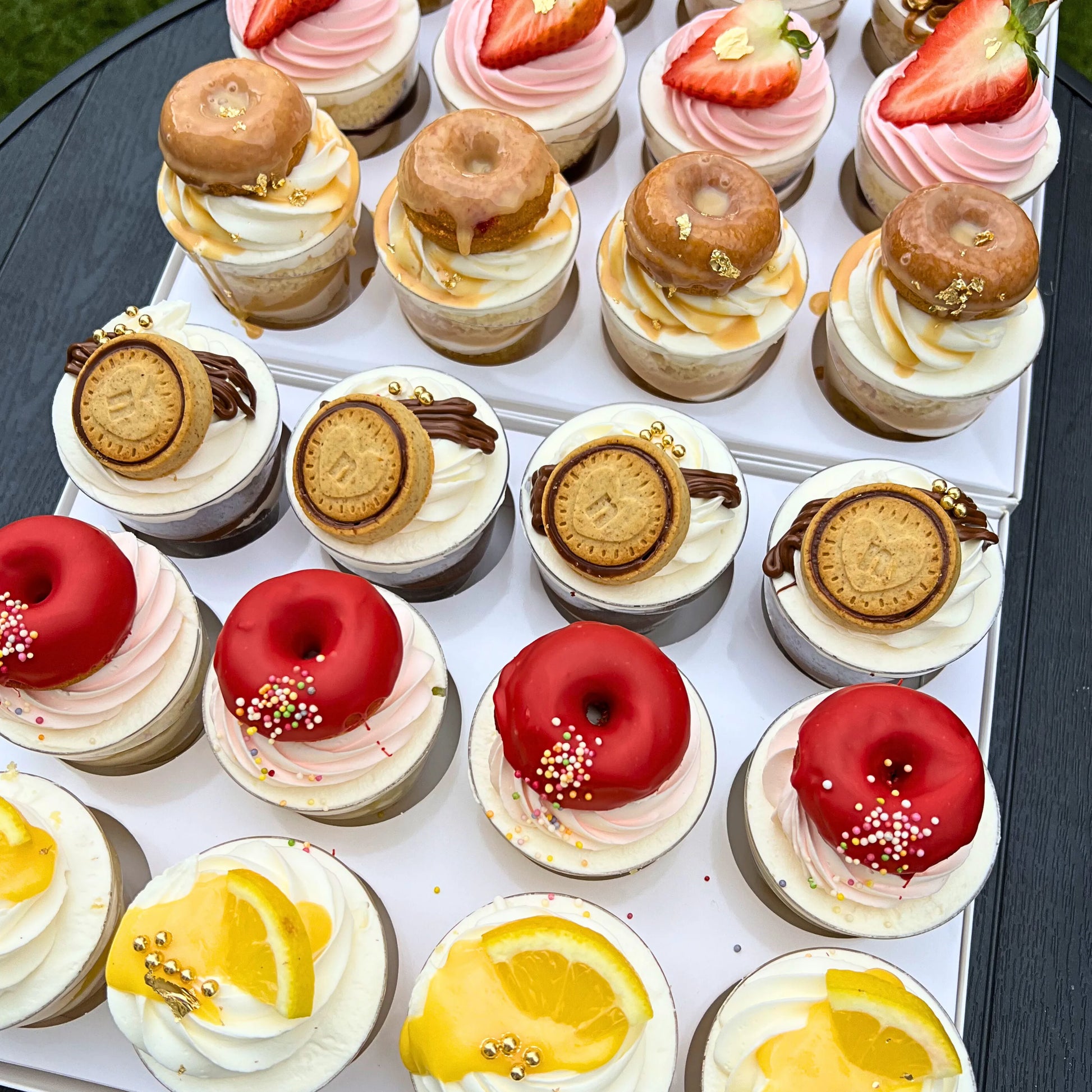 Assorted mini desserts including donut-shaped cookies and cupcakes on a white tray.