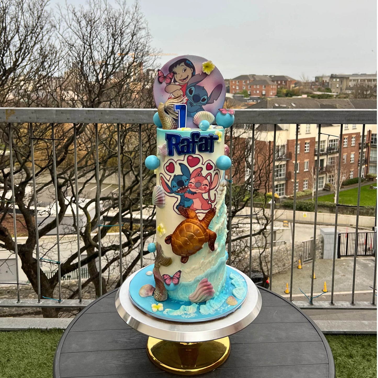 Colorful birthday cake with cartoon characters on a balcony with a cityscape background
