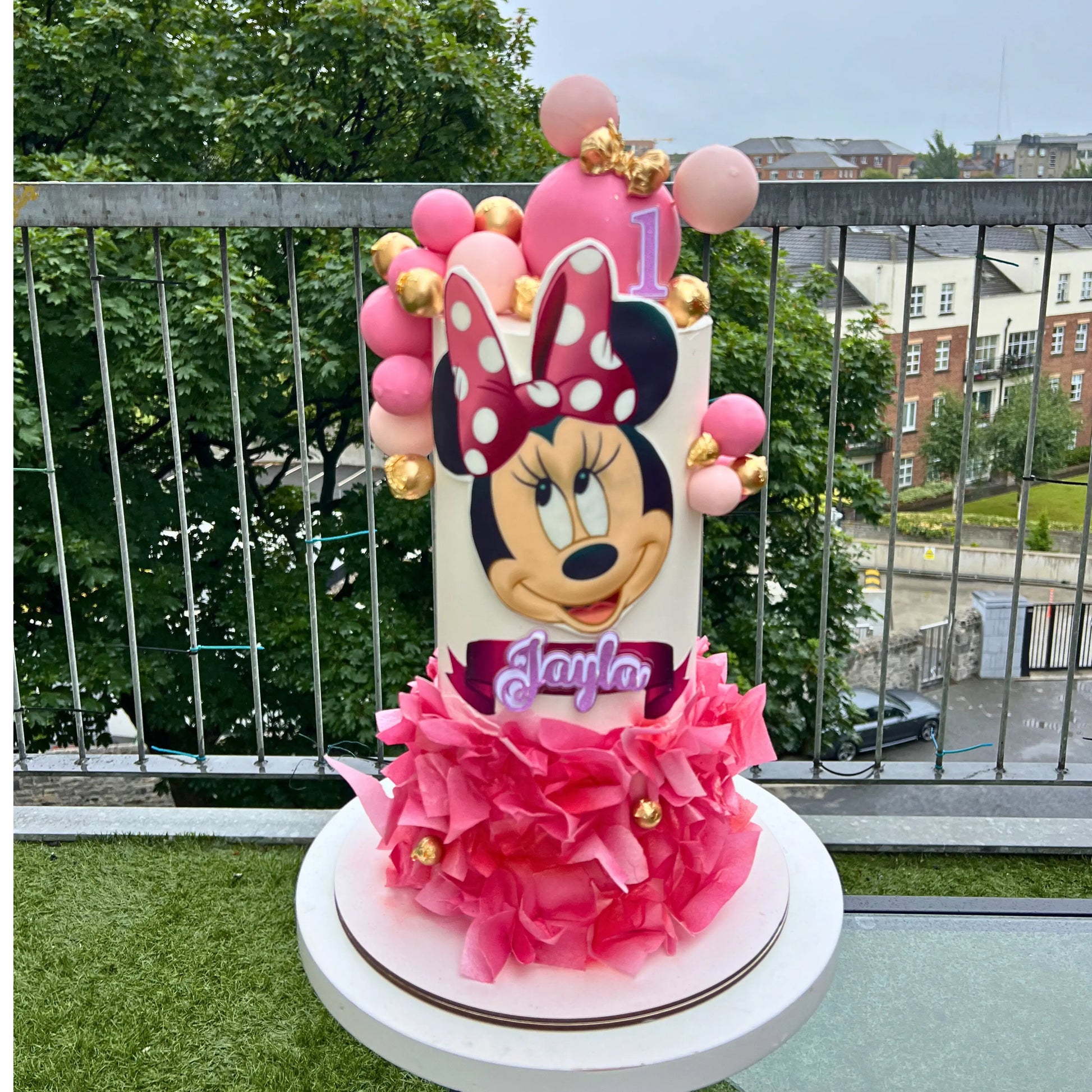 Pink Minnie Mouse-themed birthday cake with balloons on a outdoor setting