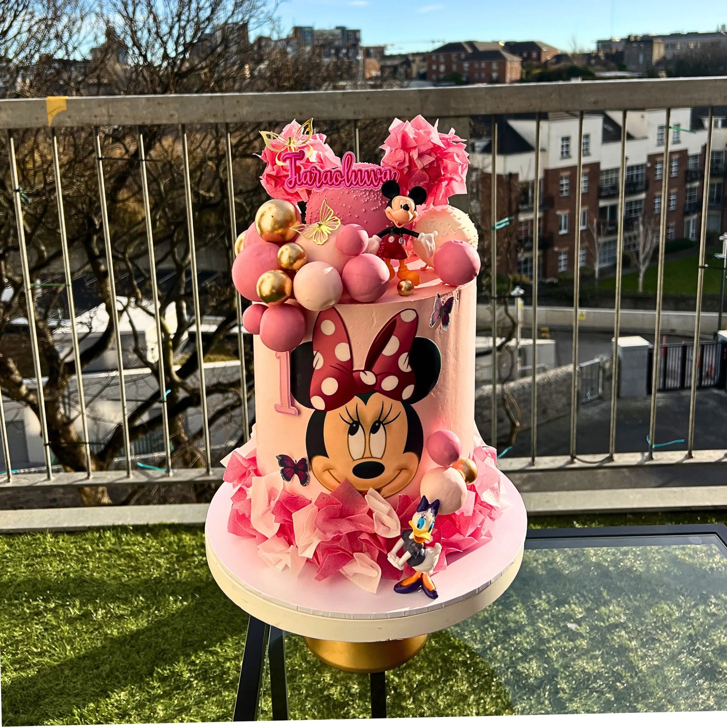 Pink Minnie Mouse-themed birthday cake with decorative elements on a balcony.