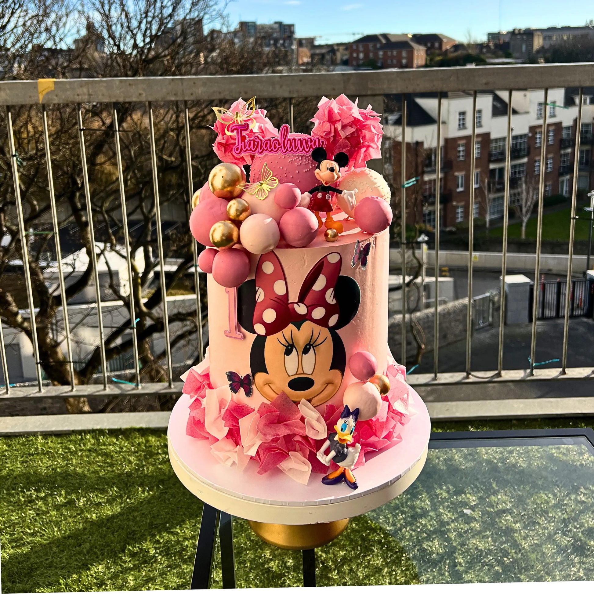 Pink Minnie Mouse-themed birthday cake with decorative elements on a balcony.