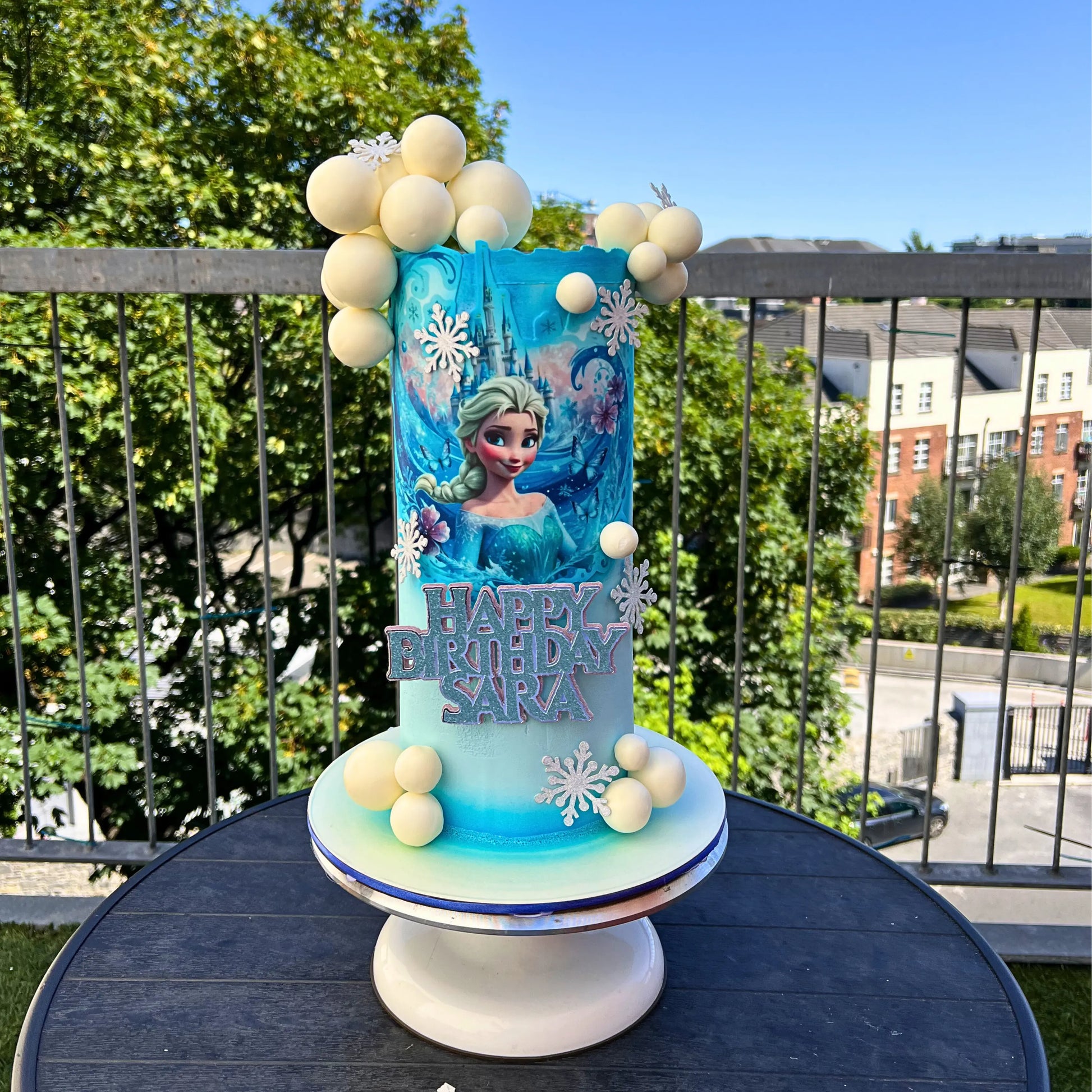 Frozen-themed birthday cake with Elsa on a stand outdoors