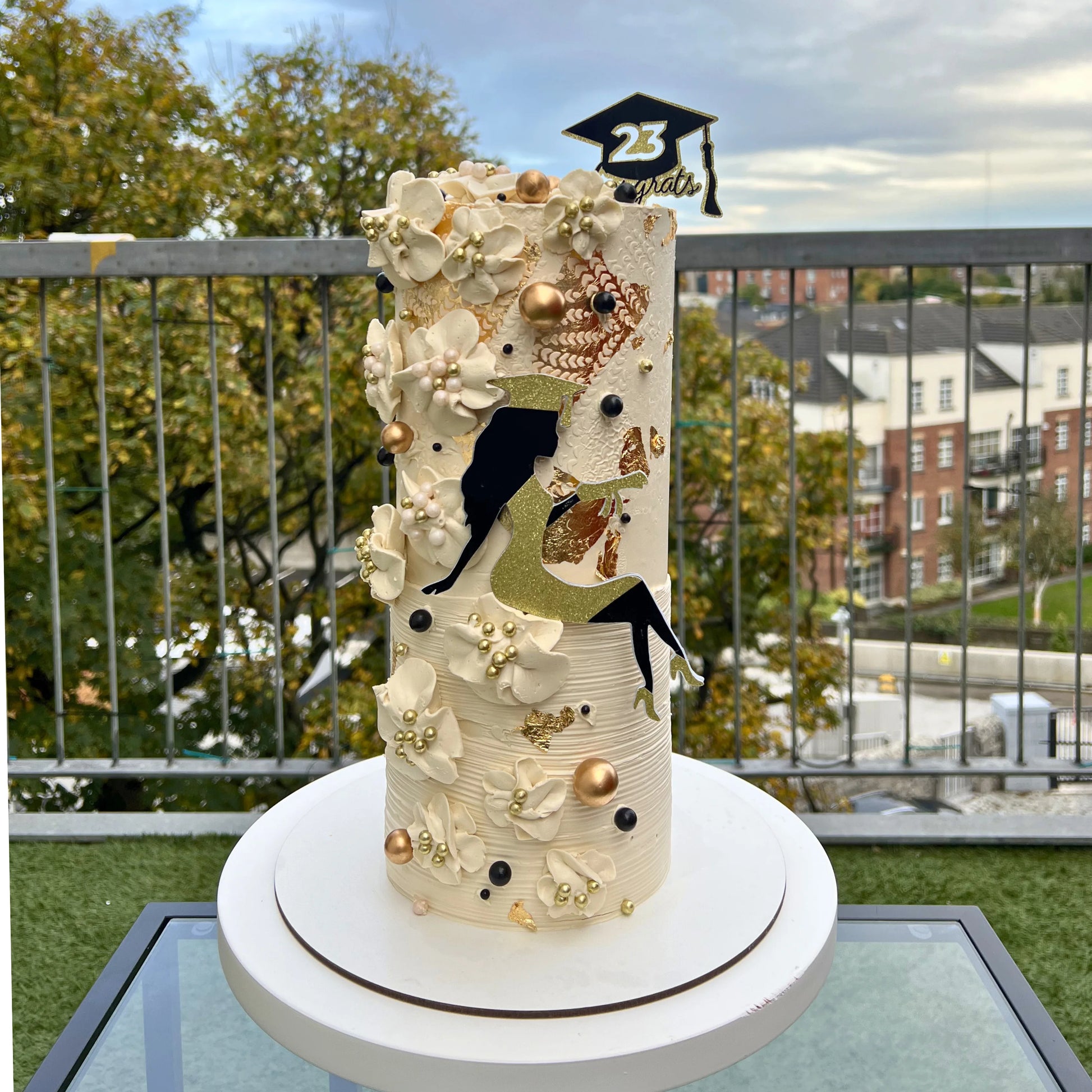 Decorative cake with a graduation theme on a table outdoors.