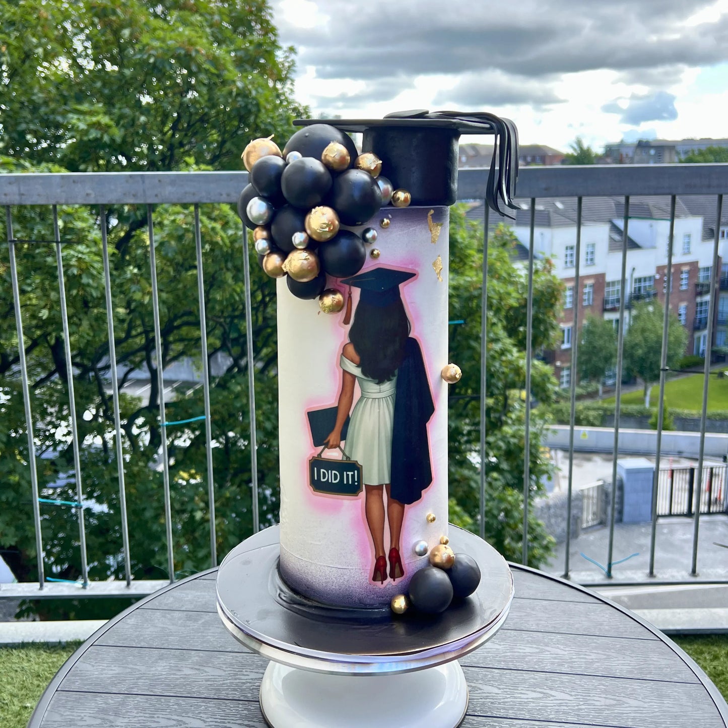 Decorative graduation-themed candle on a table with a view of trees and buildings in the background.