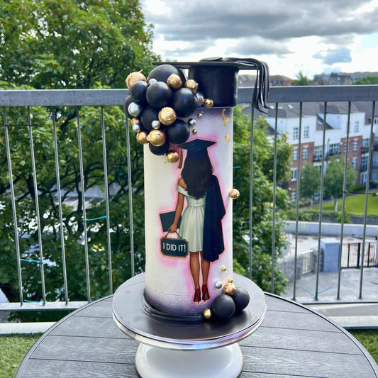 Decorative graduation-themed candle on a table with a view of trees and buildings in the background.