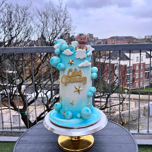 Decorative cake for a christening with blue color scheme and teddy bear on a balcony.