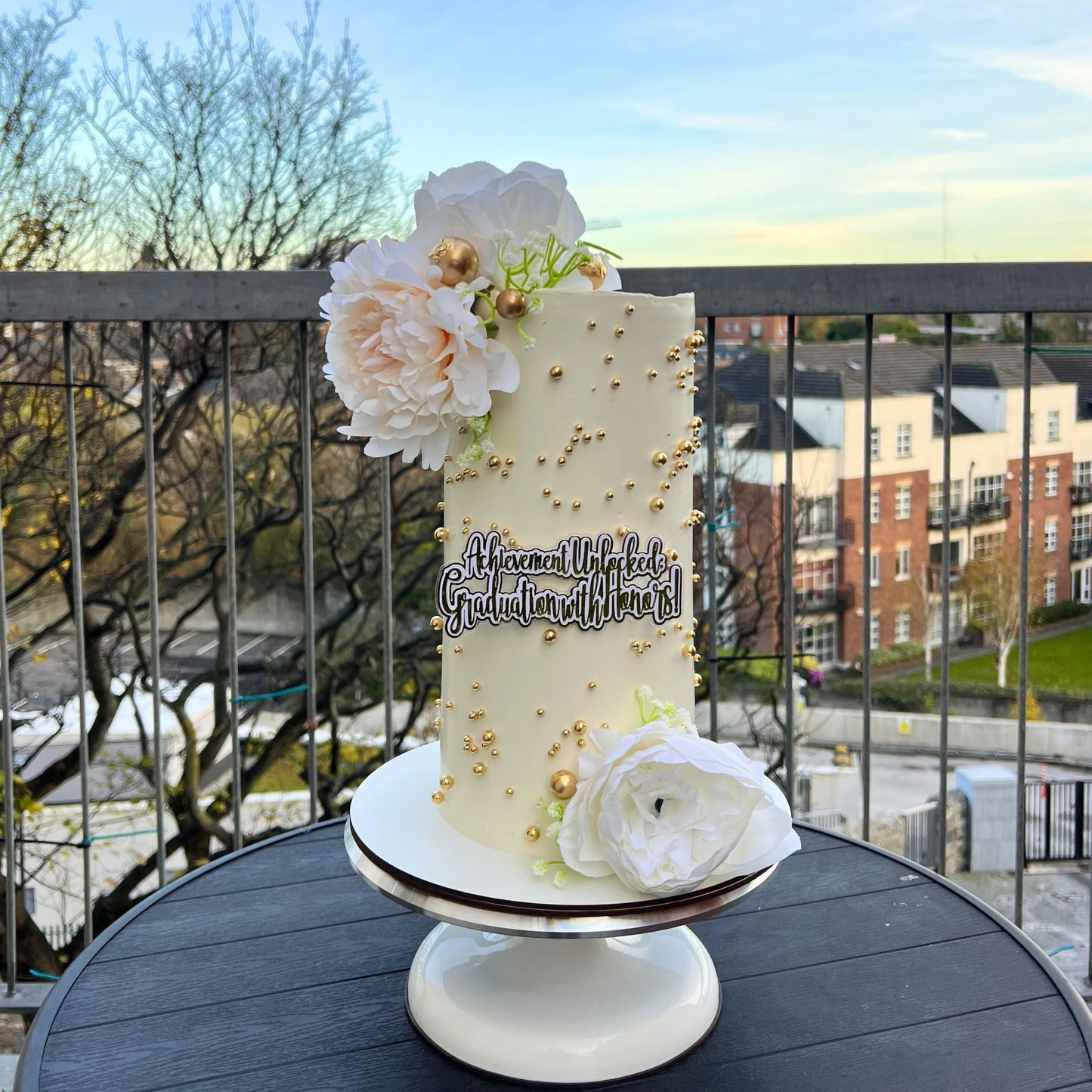 ivory birthday cake with floral decorations  with flowers on a stand outdoors