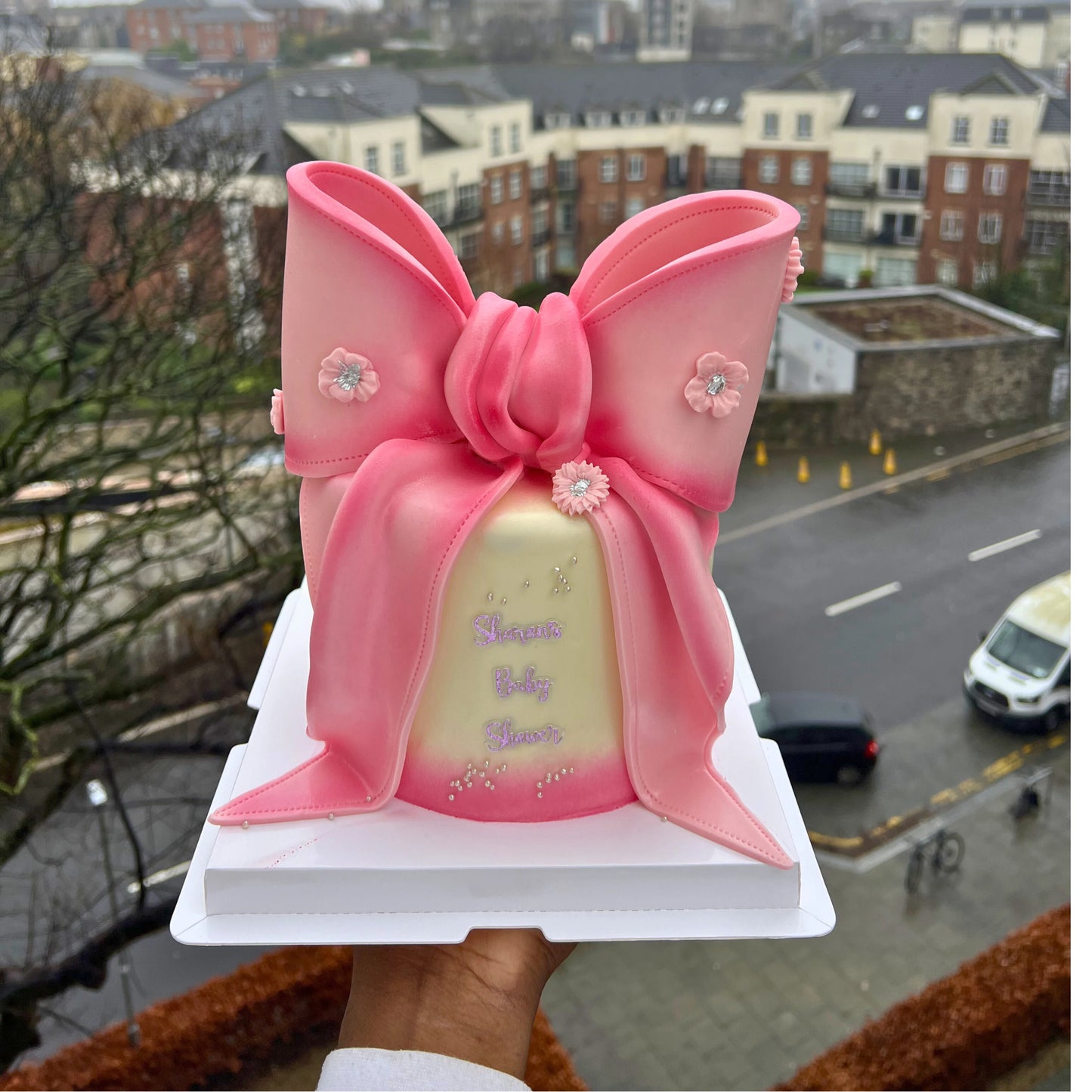 Decorative pink bow with embellishments held against a cityscape background