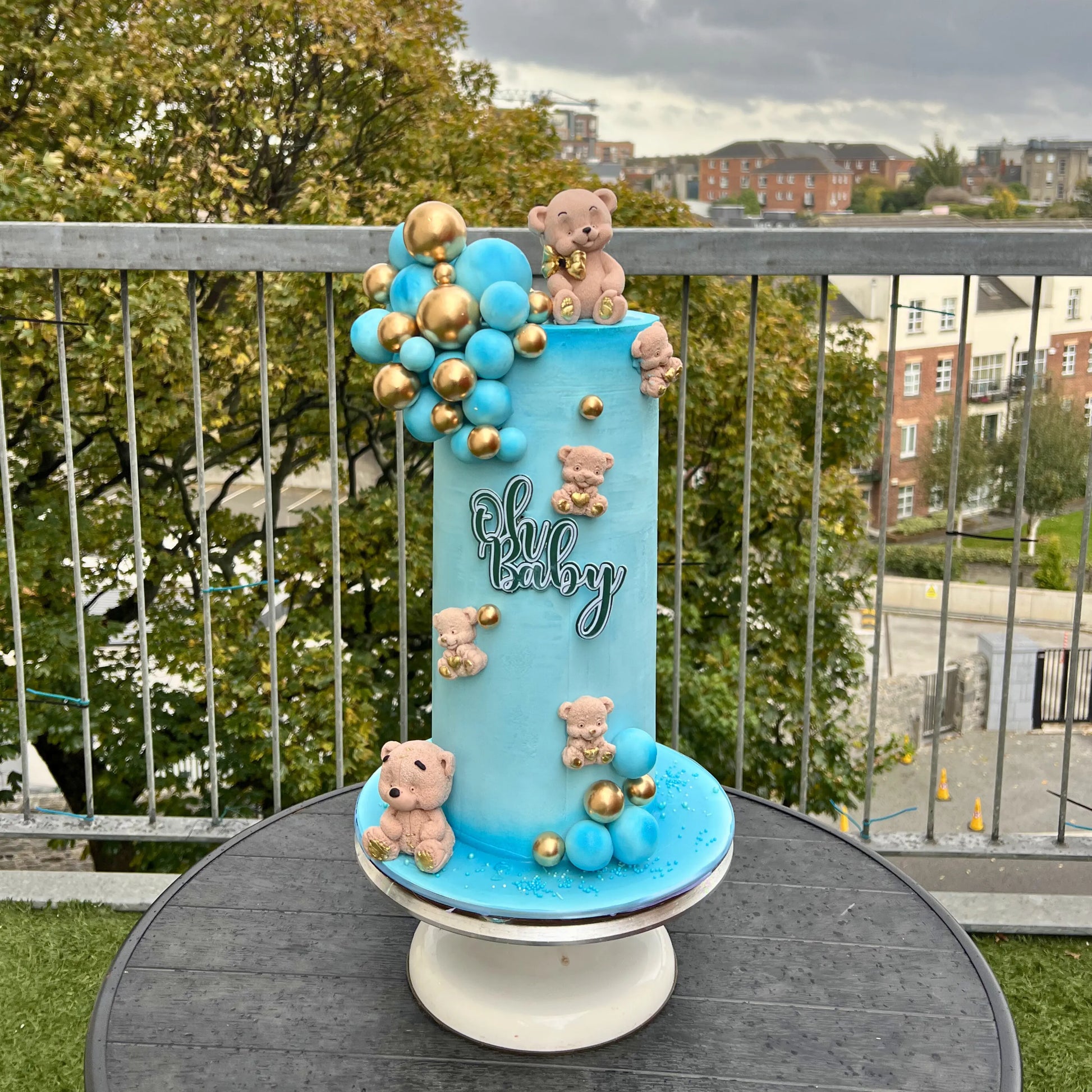 oh Baby shower cake with teddy bears and balloons on a stand outdoors.