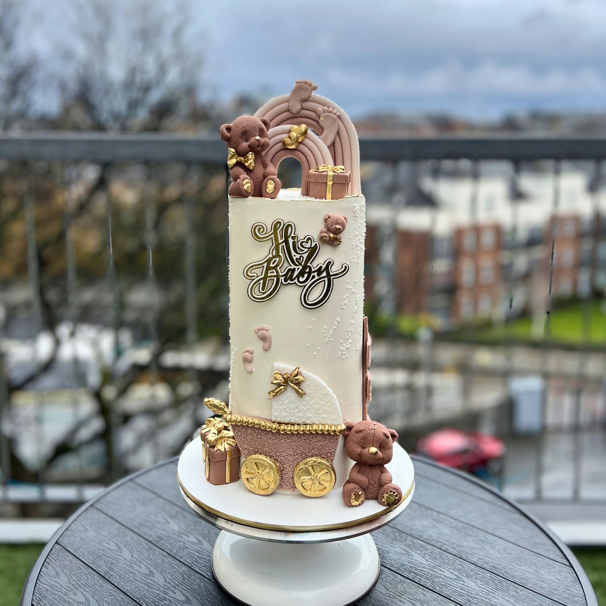 oh baby baby shower cake with baby-themed elements on a stand outdoors.