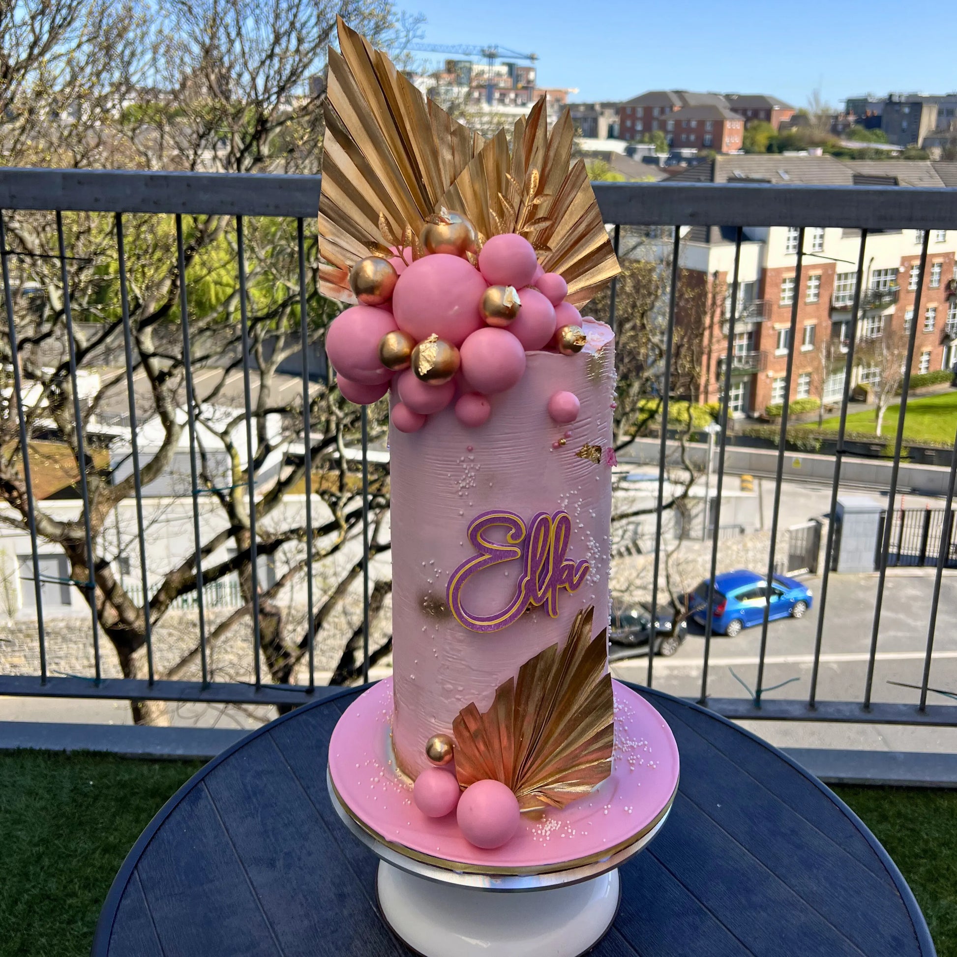 Decorative cake with pink and gold elements on a table outdoors.
