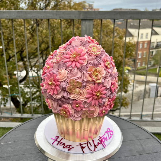 Large decorative cupcake with pink flowers on a stand outdoors.