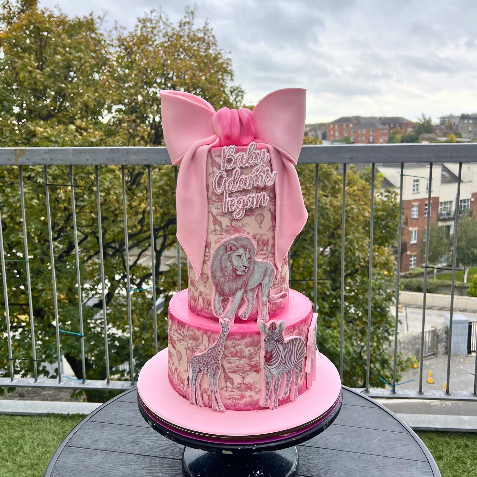 Pink baby shower cake with animal illustrations on a balcony