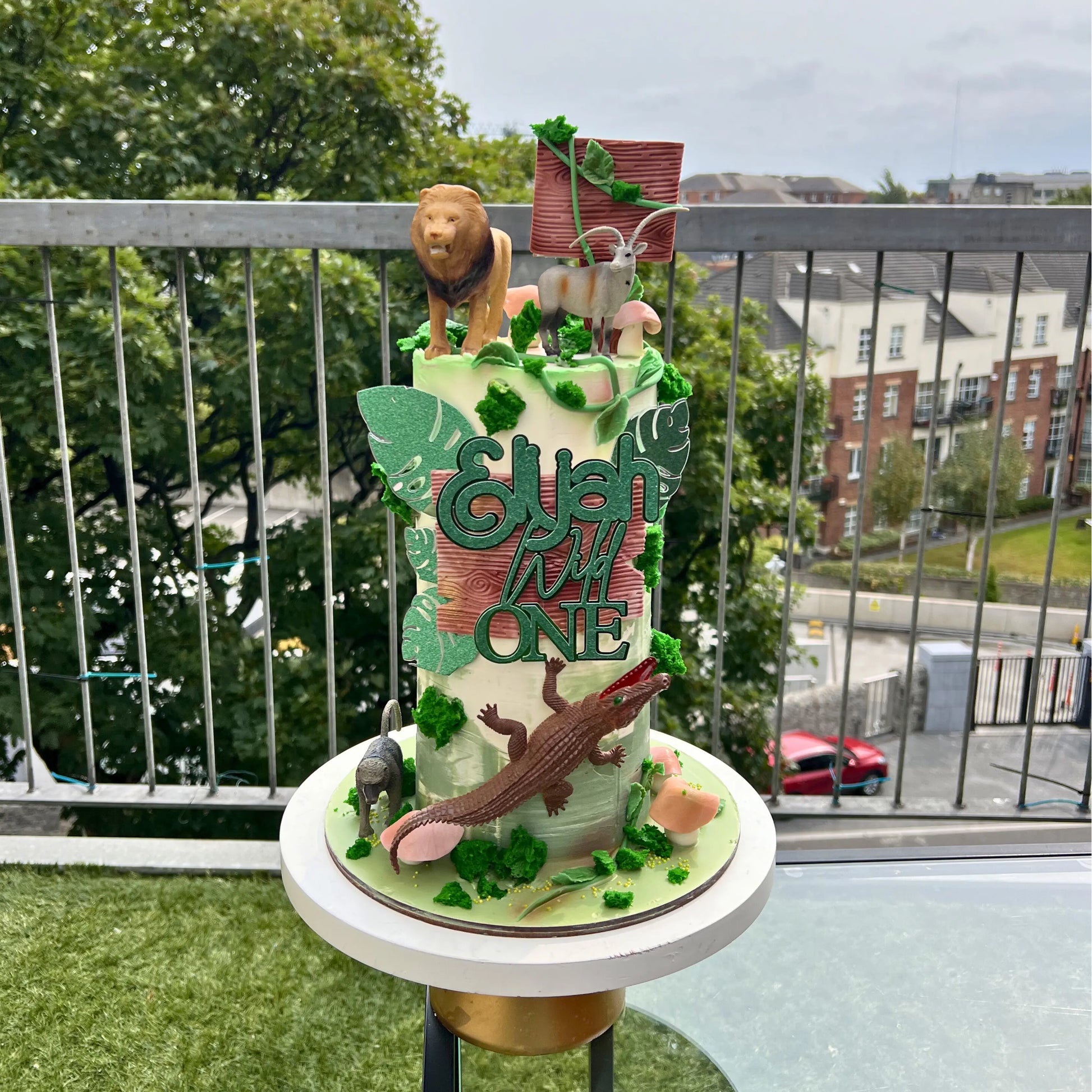 Decorative cake with animal figures and 'Happy Birthday' text on a balcony.