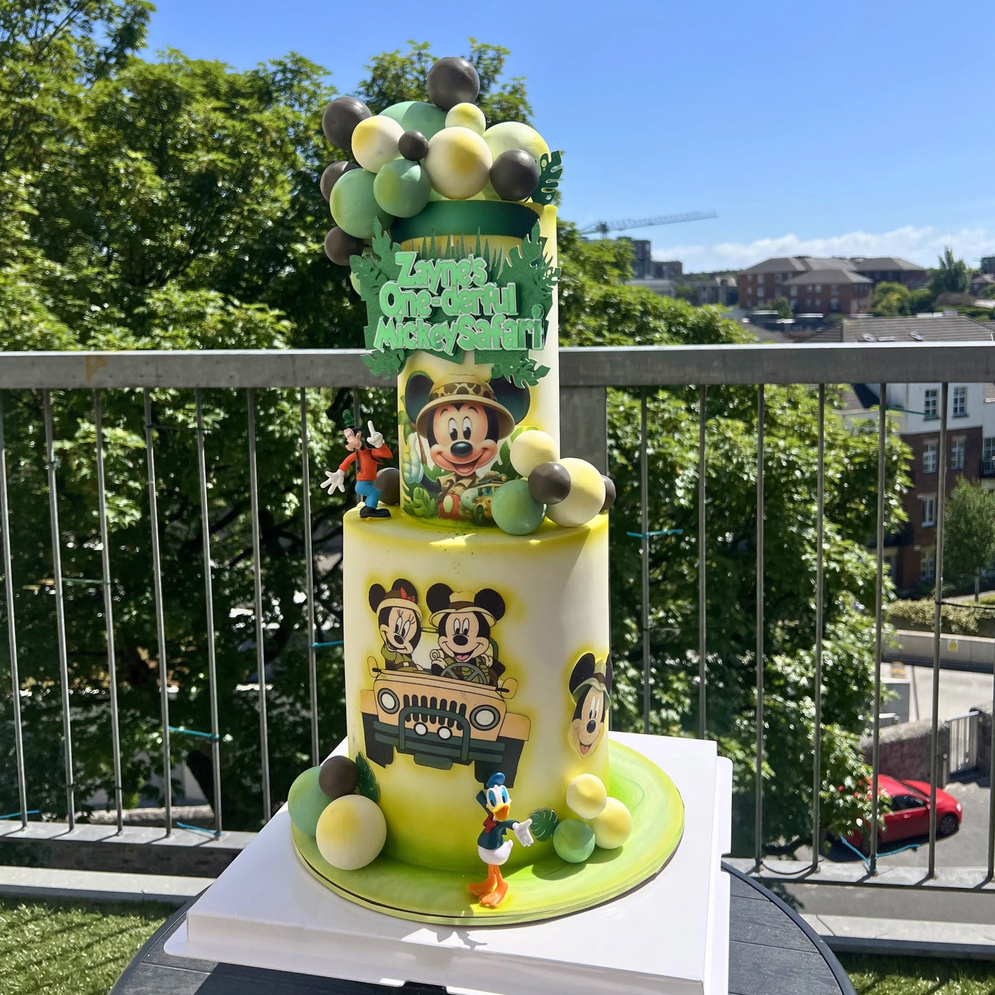 Colorful children's birthday cake with safari mickey mouse cartoon characters on a balcony