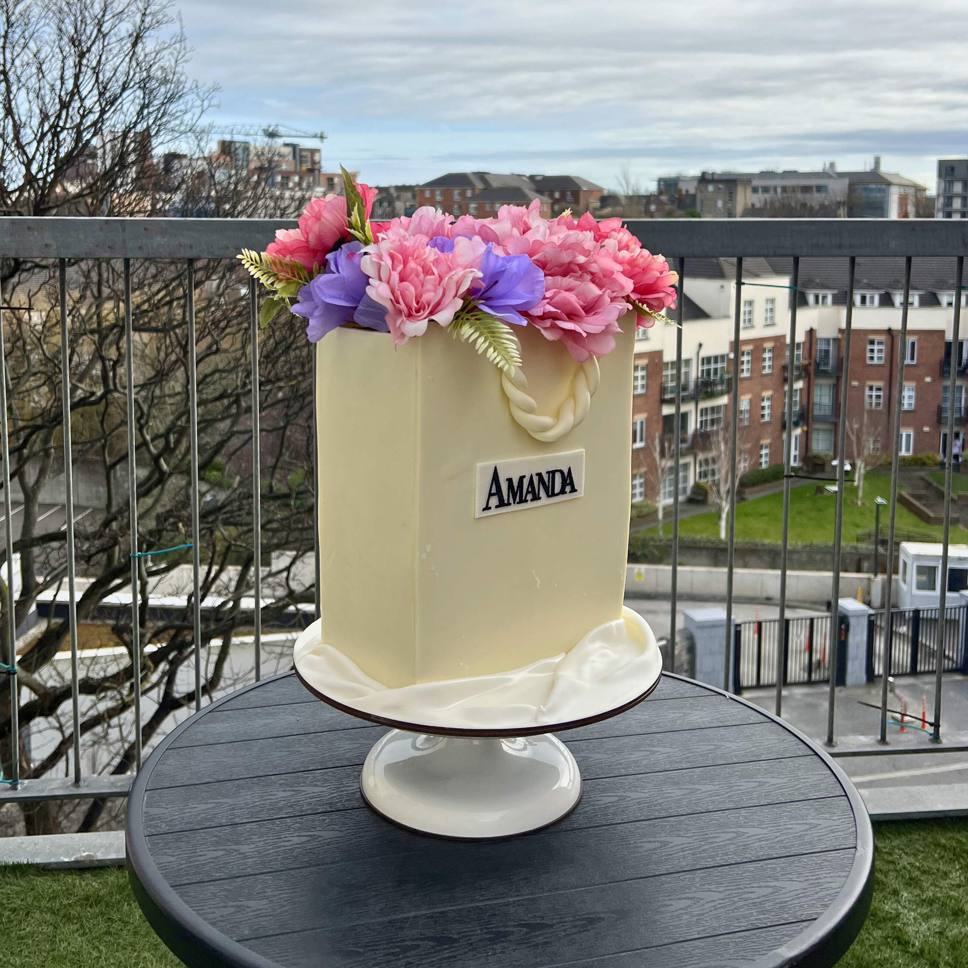 Decorative shopping bag cake with flowers on a stand outdoors