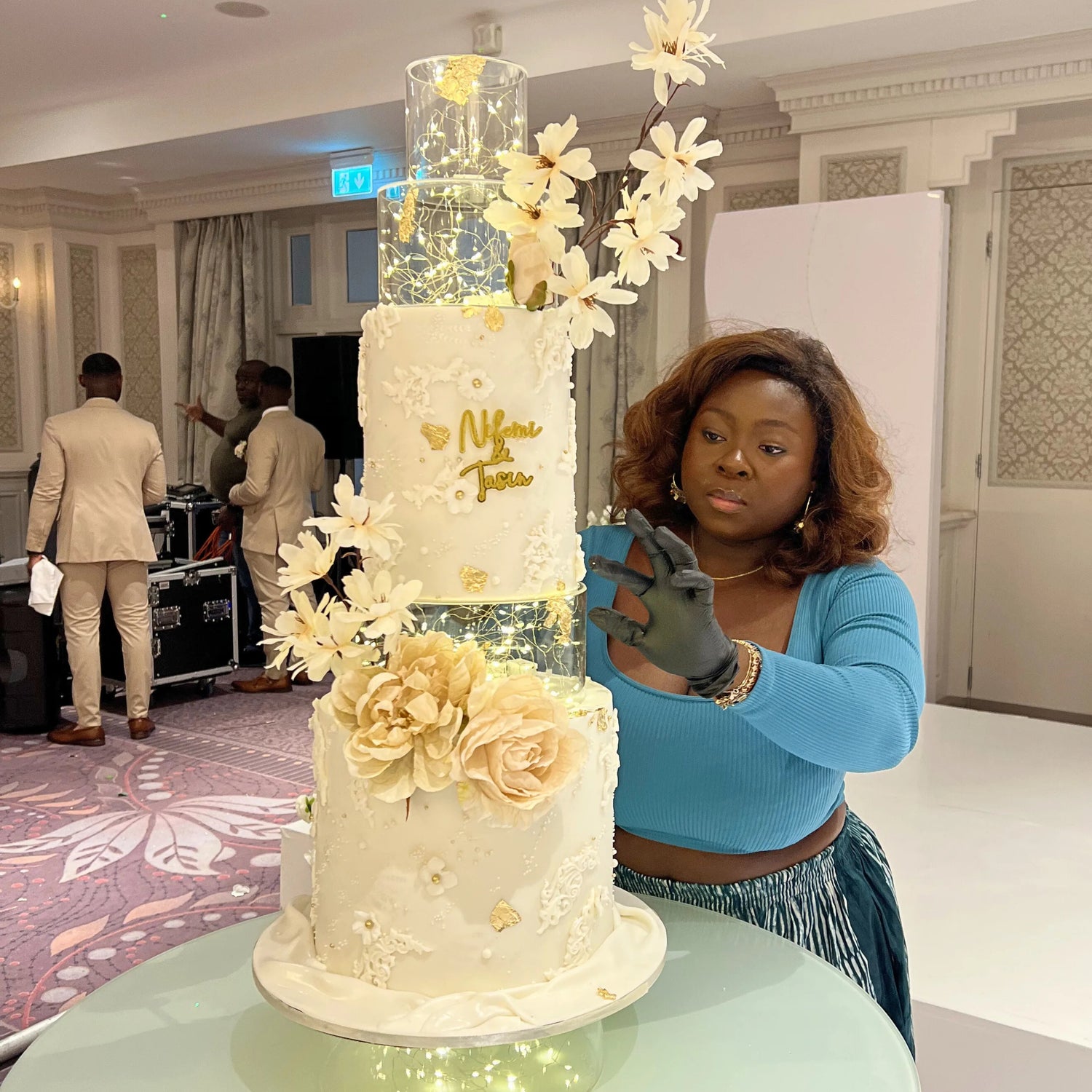 CakemeawayIE  posing with a large, decorated cake in an indoor setting